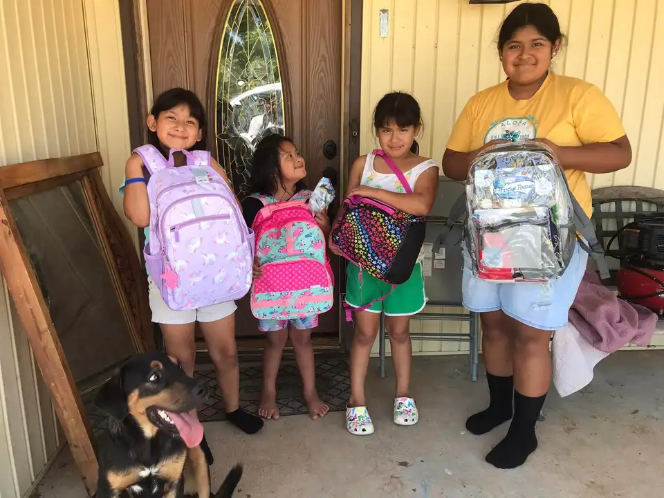 Girls showing off their new school backpacks on a front porch, with a dog at their feet