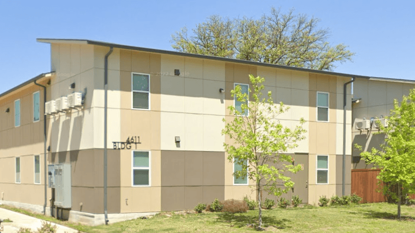 Two-story apartment buildings with a lawn and young trees