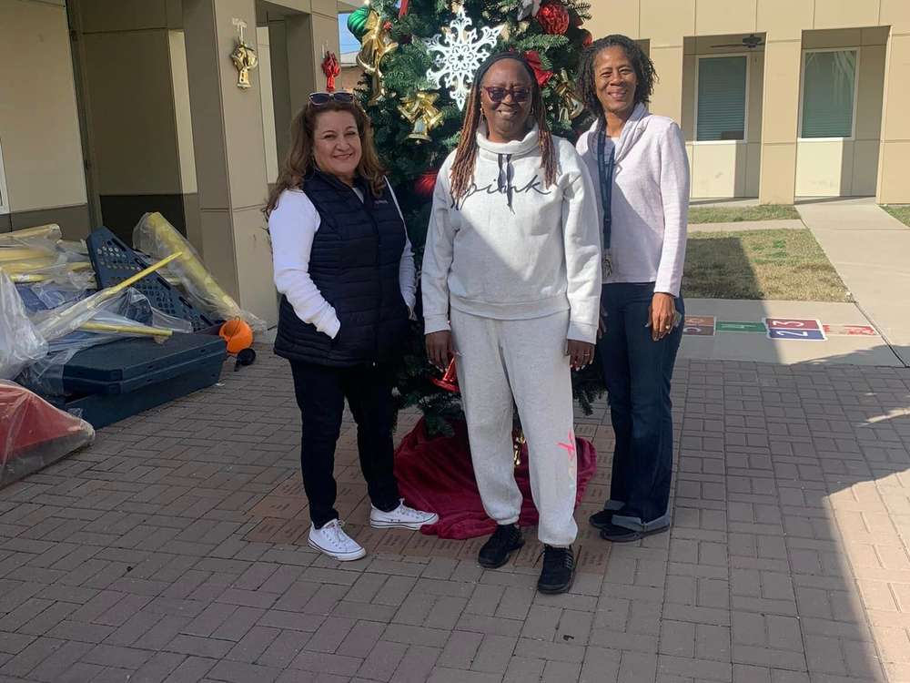 Three volunteers standing by a decorated Christmas tree outside an apartment building