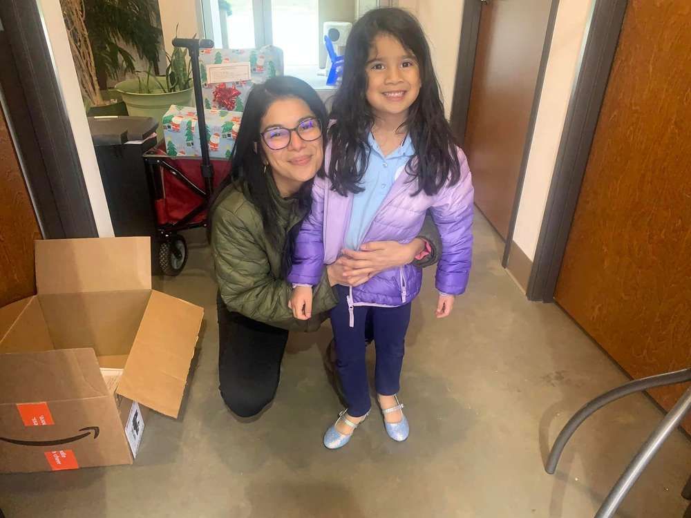 A woman kneeling next to a smiling girl in a purple jacket, with moving boxes around them