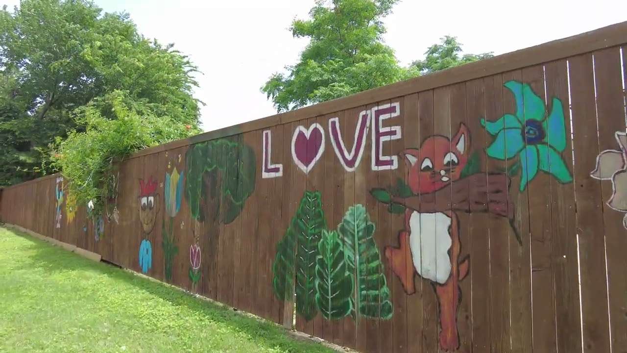 A wooden fence painted with LOVE and bright flowers beside a green lawn