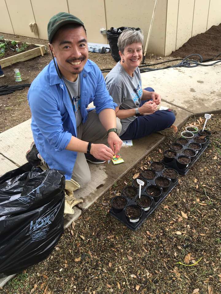 Two volunteers kneeling beside a garden bed, planting seedlings