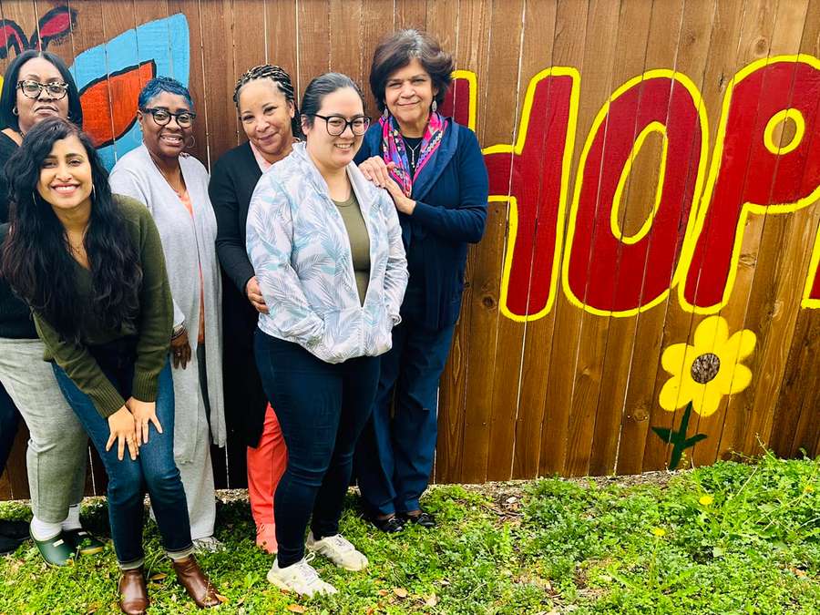 A group of women standing together in front of a colorful mural that says HOPE
