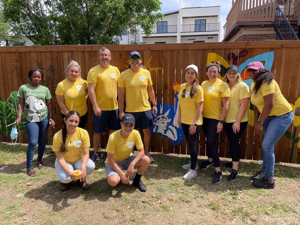 Volunteers in matching yellow T-shirts in front of a fence painted with bright murals